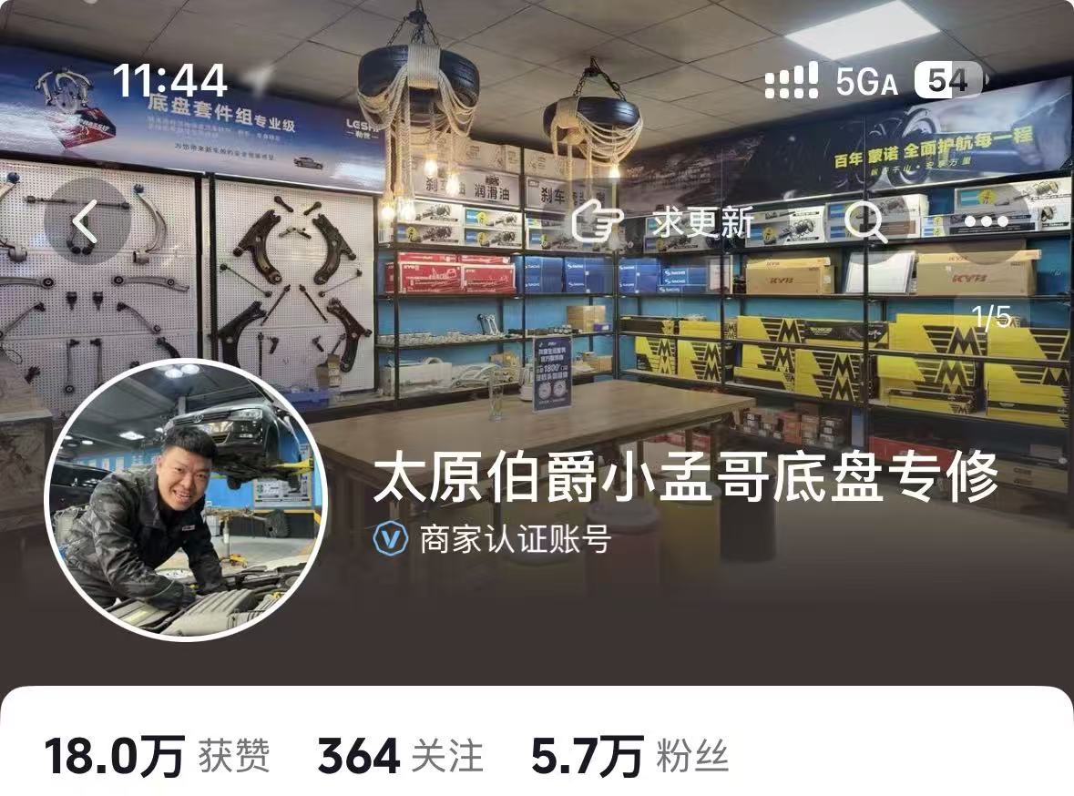 中年男性老板站在汽修店门口，面带微笑，身穿深色夹克，背景是店面招牌和停靠的几辆汽车，阳光明媚